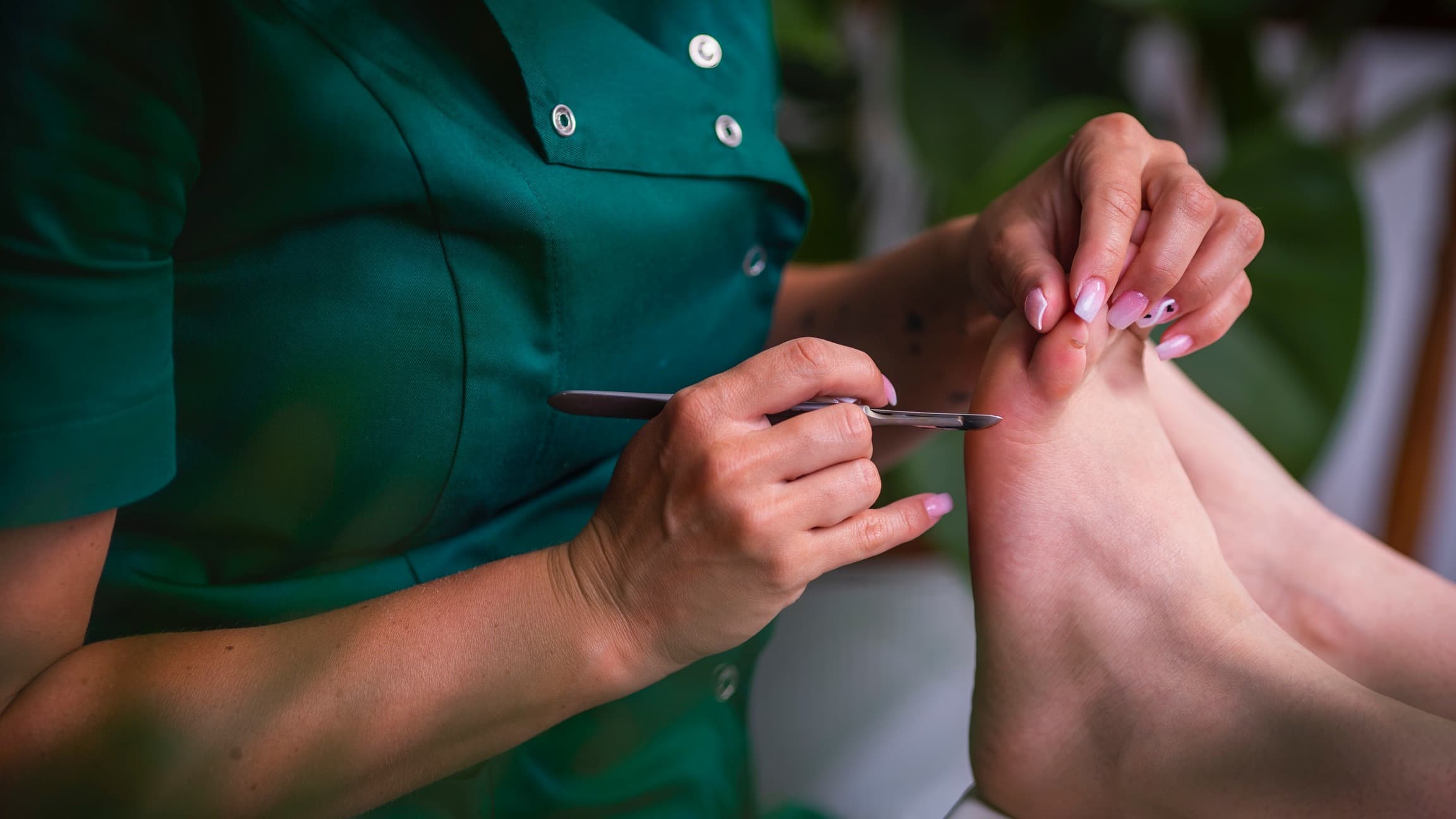 zblizenie na stopy i reke kosmetologa trzymajaca skalpel w trakcie zabiegu pedicure podologiczny w salonie kosmetycznym