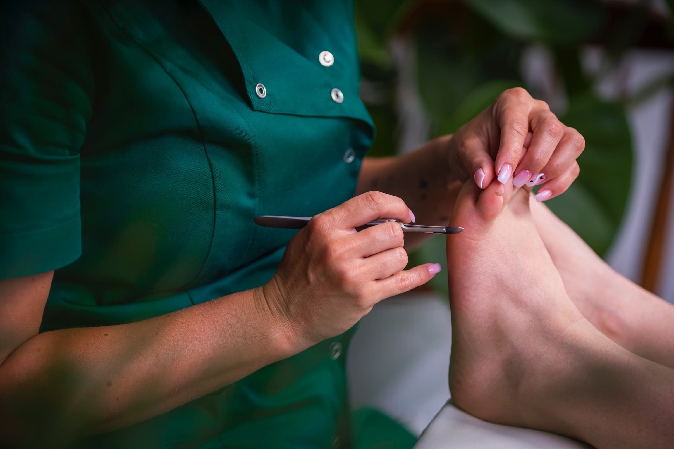 zbliżenie na stopy i rękę kosmetologa trzymającą skalpel w trakcie zabiegu pedicure podologiczny w salonie kosmetycznym Health and beauty w Krakowie