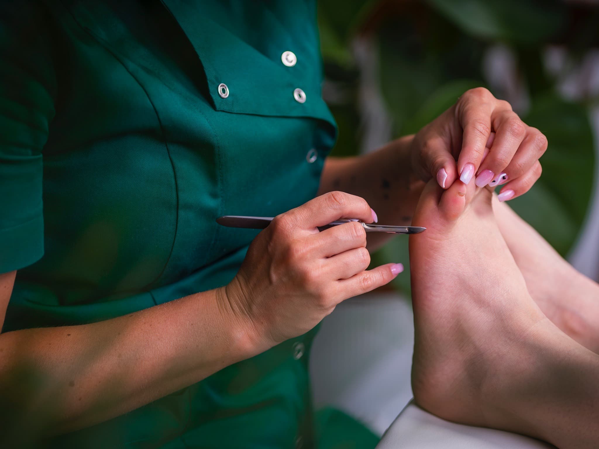 zbliżenie na stopy i rękę kosmetologa trzymającą skalpel w trakcie zabiegu pedicure podologiczny w salonie kosmetycznym Health and beauty w Krakowie